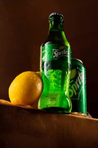 Sprite bottle and can with fresh lemon and water droplets for a vibrant visual.